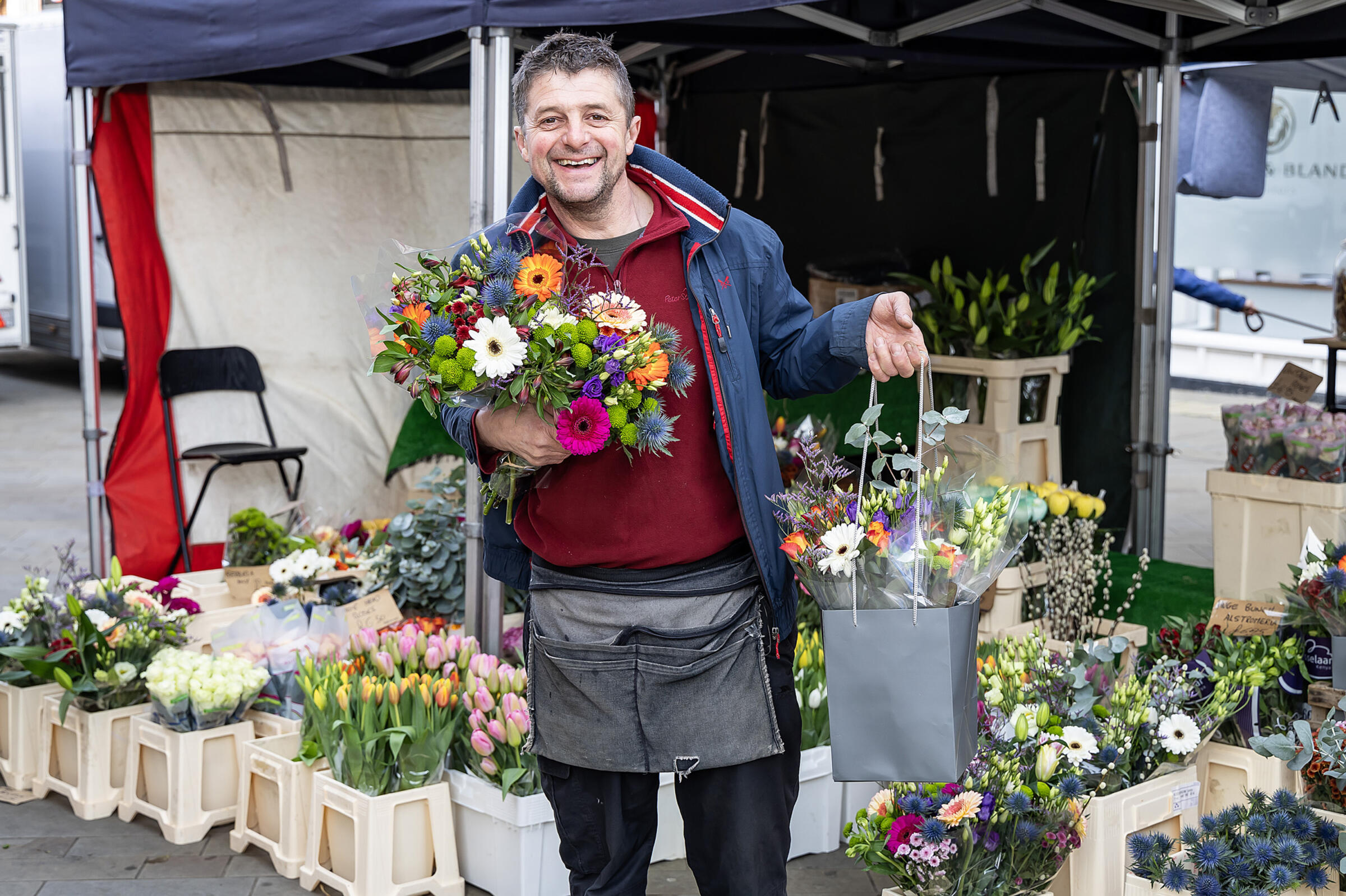 Trader with flowers standing by a flower stall